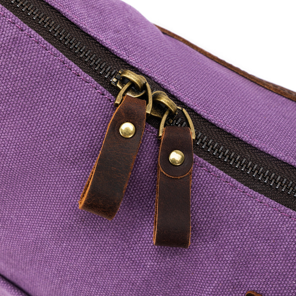 Close-up of a purple bag with a black zipper and brown leather pull tabs.