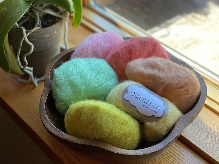 A selection of colorful yarn in various shades, displayed in a bowl, with a label showing the brand 'Cumulus'.