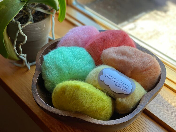 A selection of colorful yarn in various shades, displayed in a bowl, with a label showing the brand 'Cumulus'.