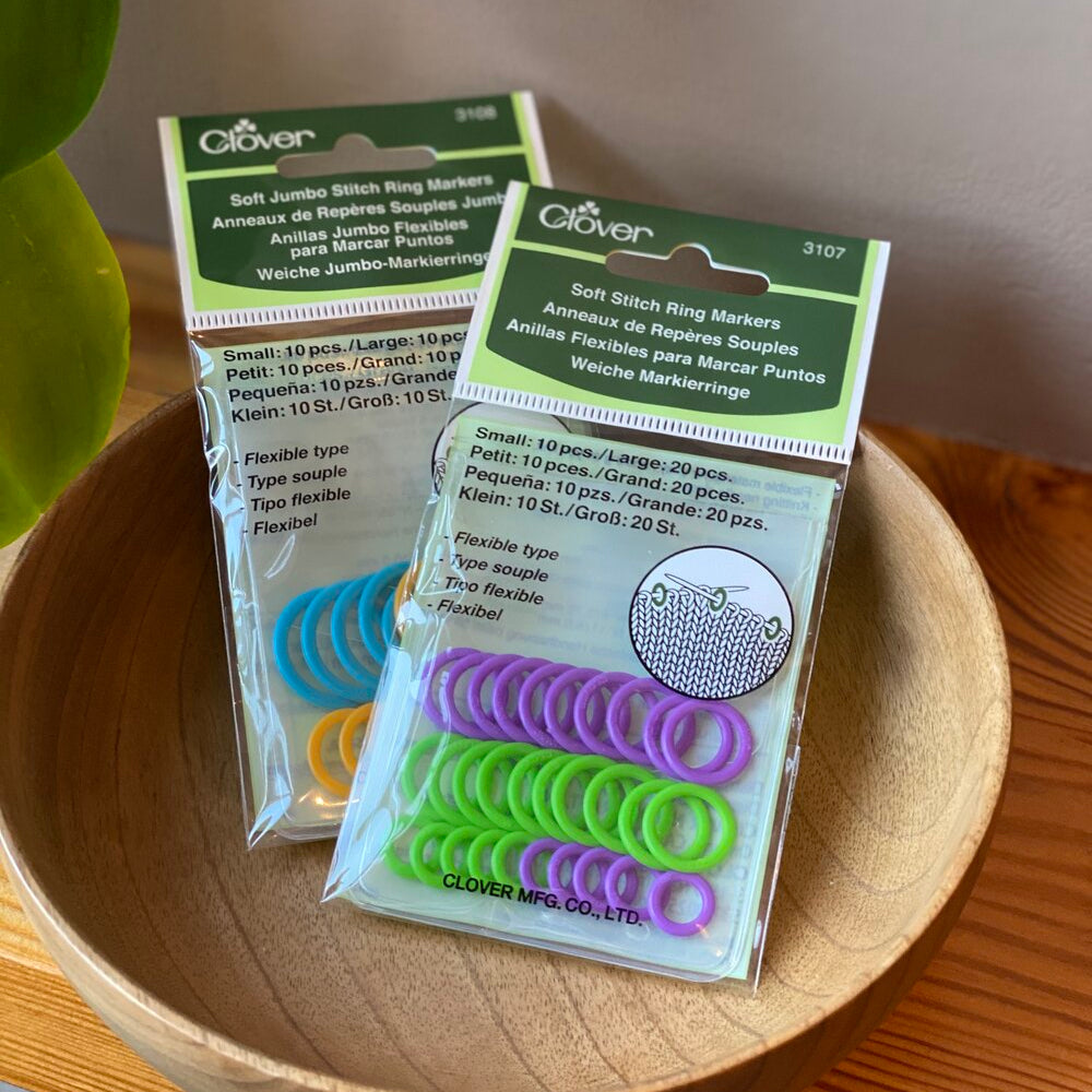 Packaging of Clover soft stitch ring markers displayed in a wooden bowl, with visible green and purple markers.