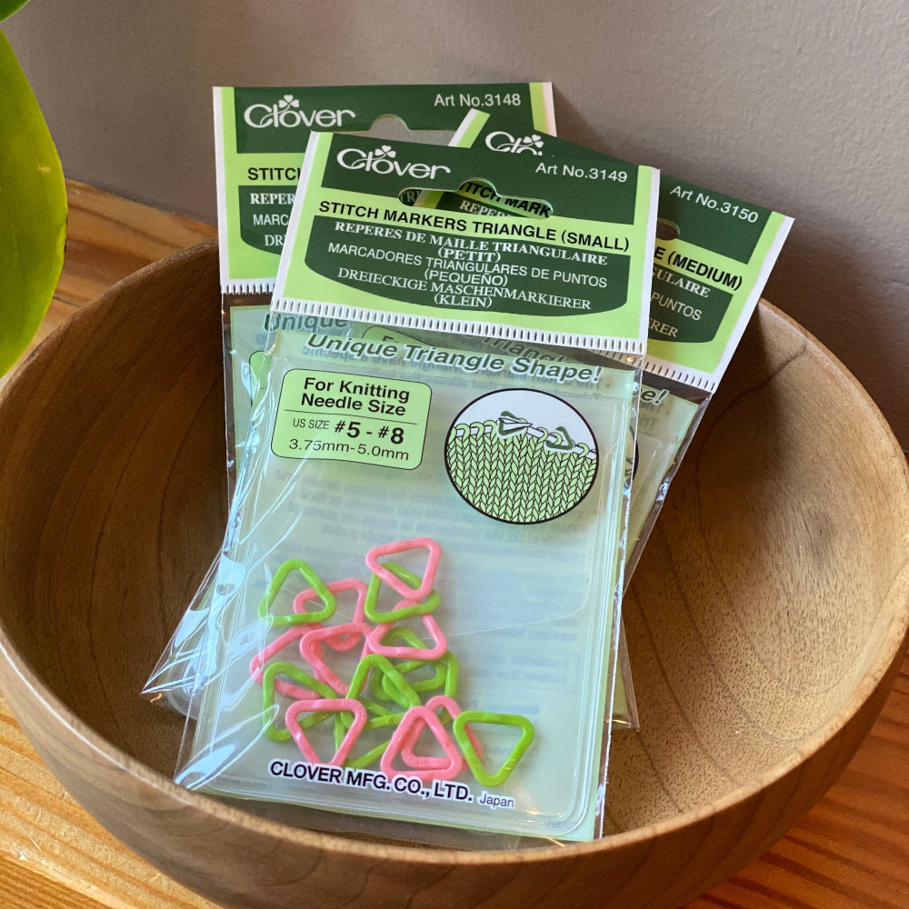 Pack of Clover brand triangle stitch markers in various sizes displayed in a wooden bowl.