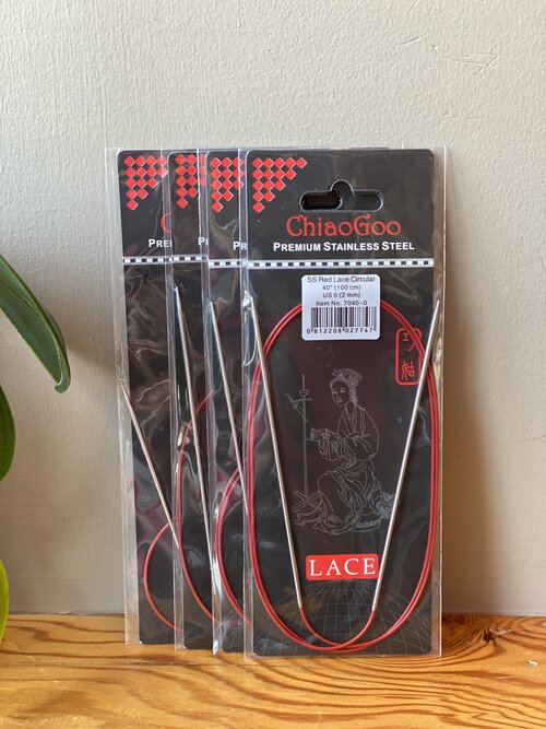 Packaged Chiaogoo Red Lace Circular knitting needles made from stainless steel, displayed on a wooden surface with a plant in the background.