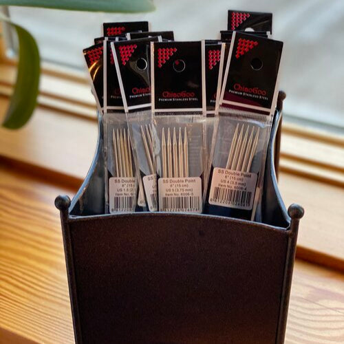 A set of Chiaogoo stainless steel double point needles displayed in an organized manner in a metal basket, with packaging visible.