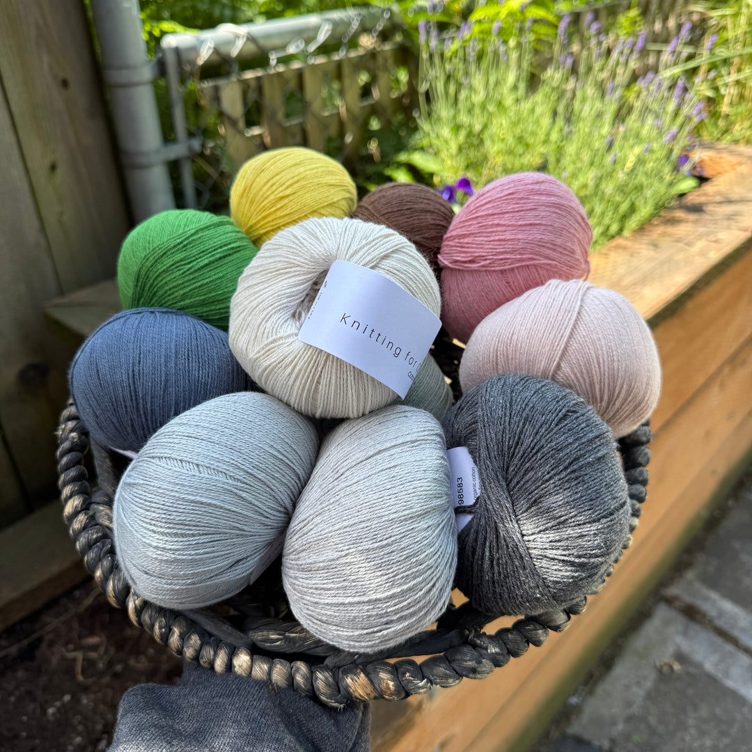 Basket of colorful yarn balls with 'Knitting for Olive Cotton Merino' label outdoors