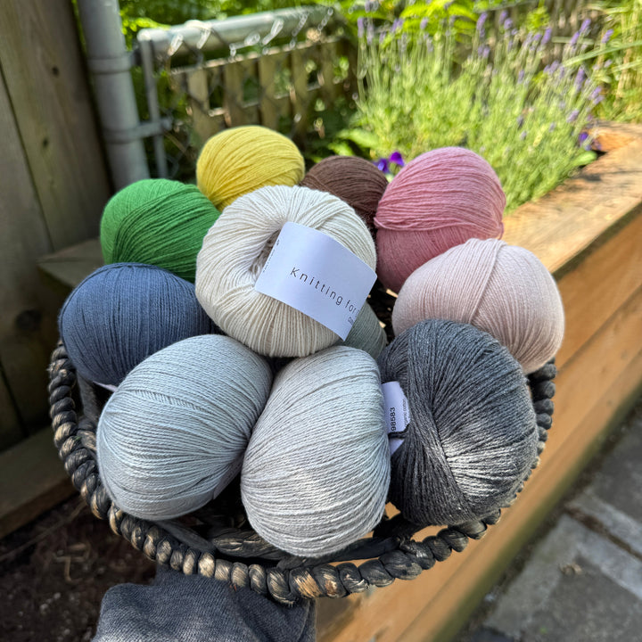 Basket of colorful yarn balls with 'Knitting for Olive Cotton Merino' label outdoors