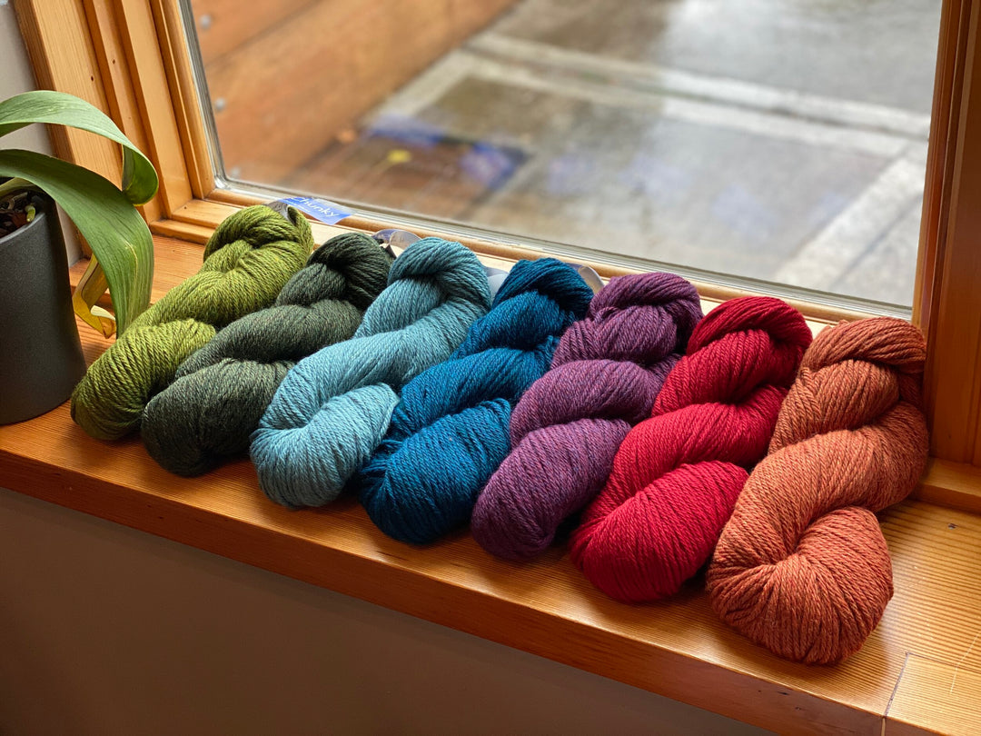 A collection of skeins of Vintage Chunky yarn arranged in a row on a windowsill, displaying a range of colors including green, blue, purple, red, and orange.