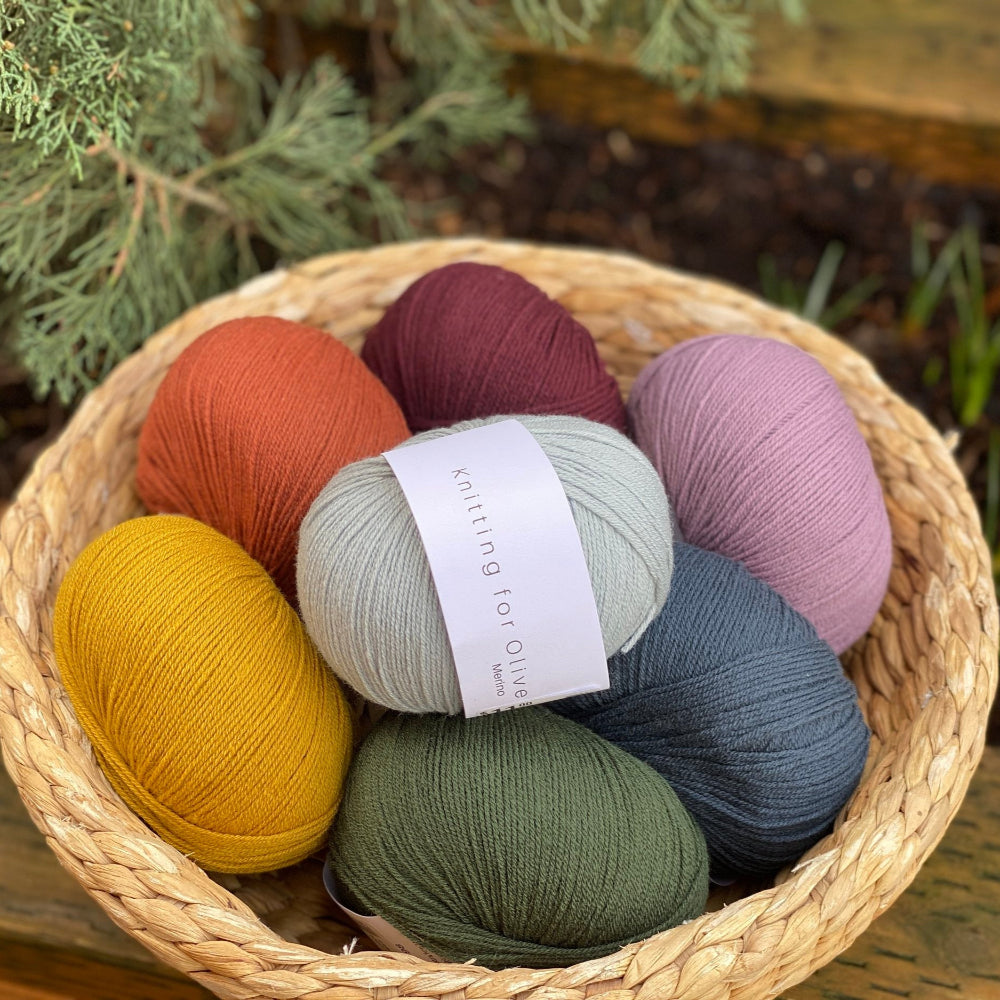 A basket containing multiple skeins of knitting for olive merino wool yarn in various colors.