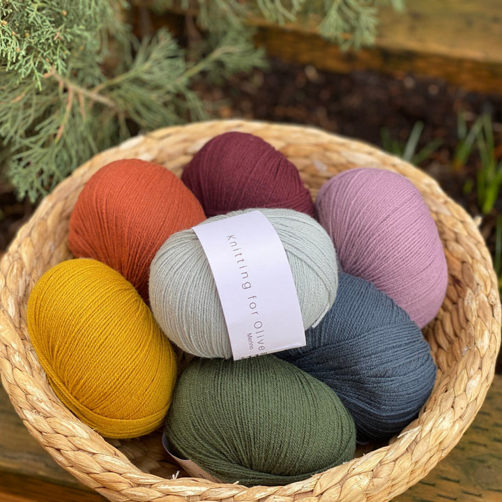 A basket containing multiple skeins of knitting for olive merino wool yarn in various colors.