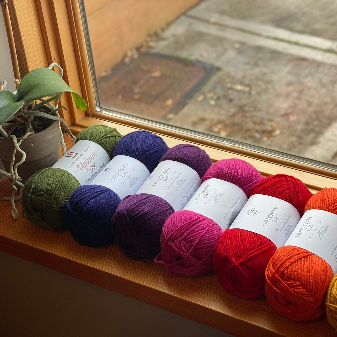 A selection of colorful Uptown DK yarn skeins arranged in a row on a windowsill.