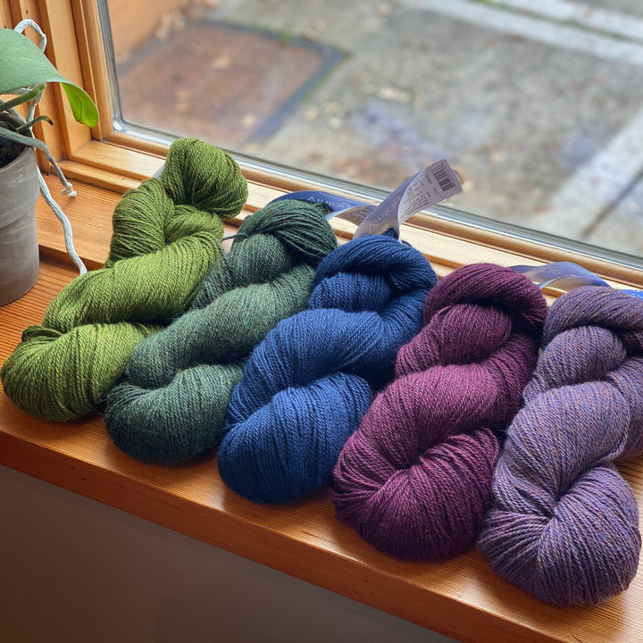 Skeins of dk weight yarn in various colors displayed on a window sill.