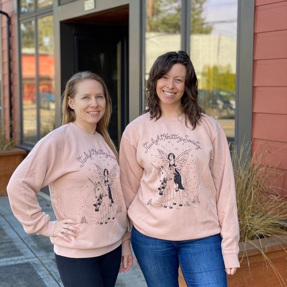 Two people standing side by side, wearing pink sweatshirts with a graphic design of a woman and a unicorn.