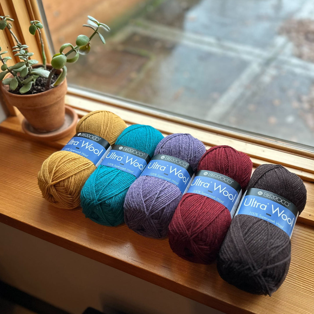 A series of skeins of Ultra Wool yarn arranged in a row on a windowsill, displaying a range of colors.