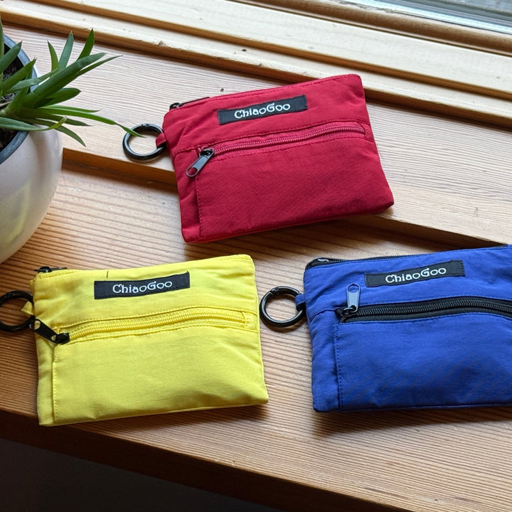 Three zippered pouches with ChiaoGoo branding, in red, yellow, and blue colors, placed on a wooden surface.