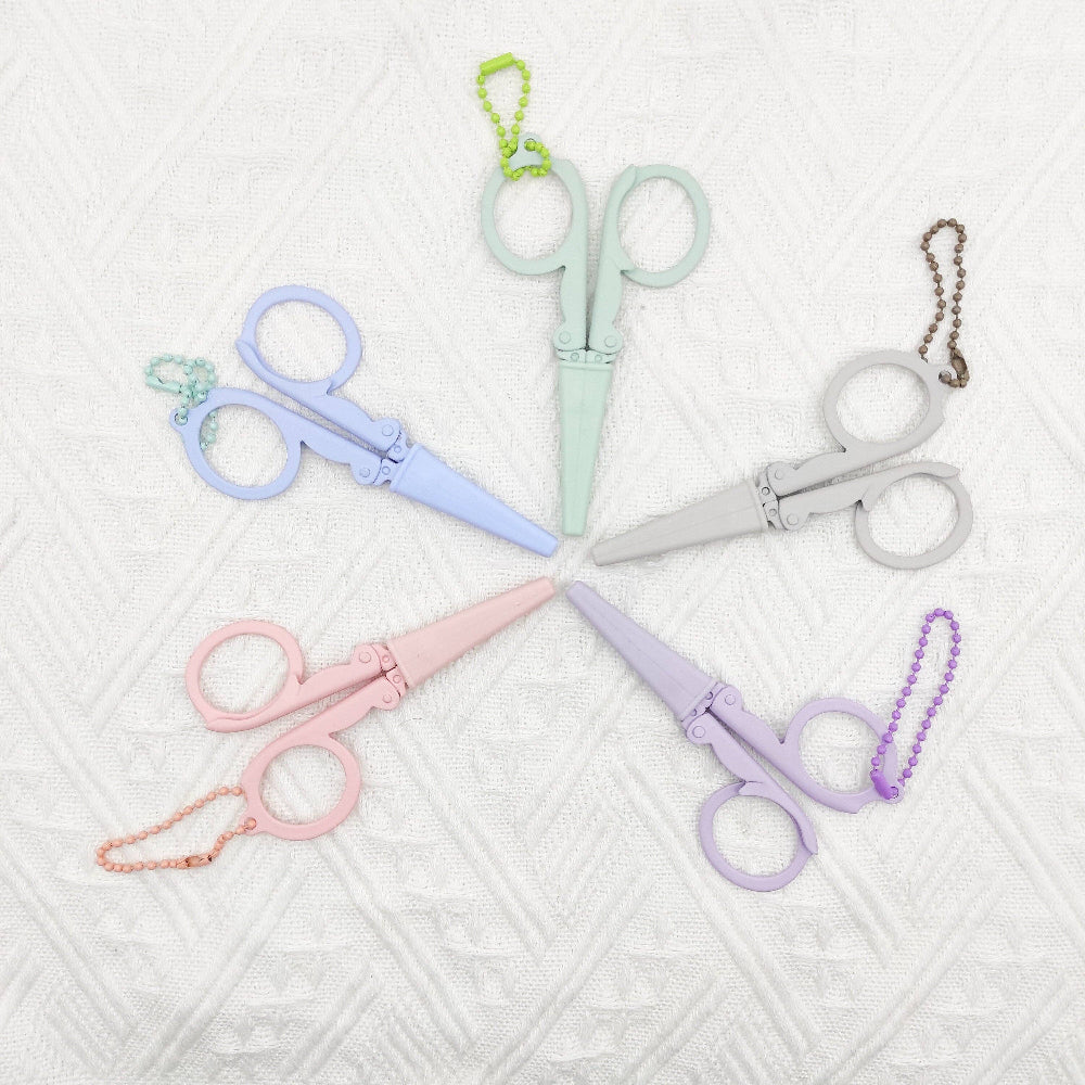 Set of pastel-colored scissors with chains on a textured white background