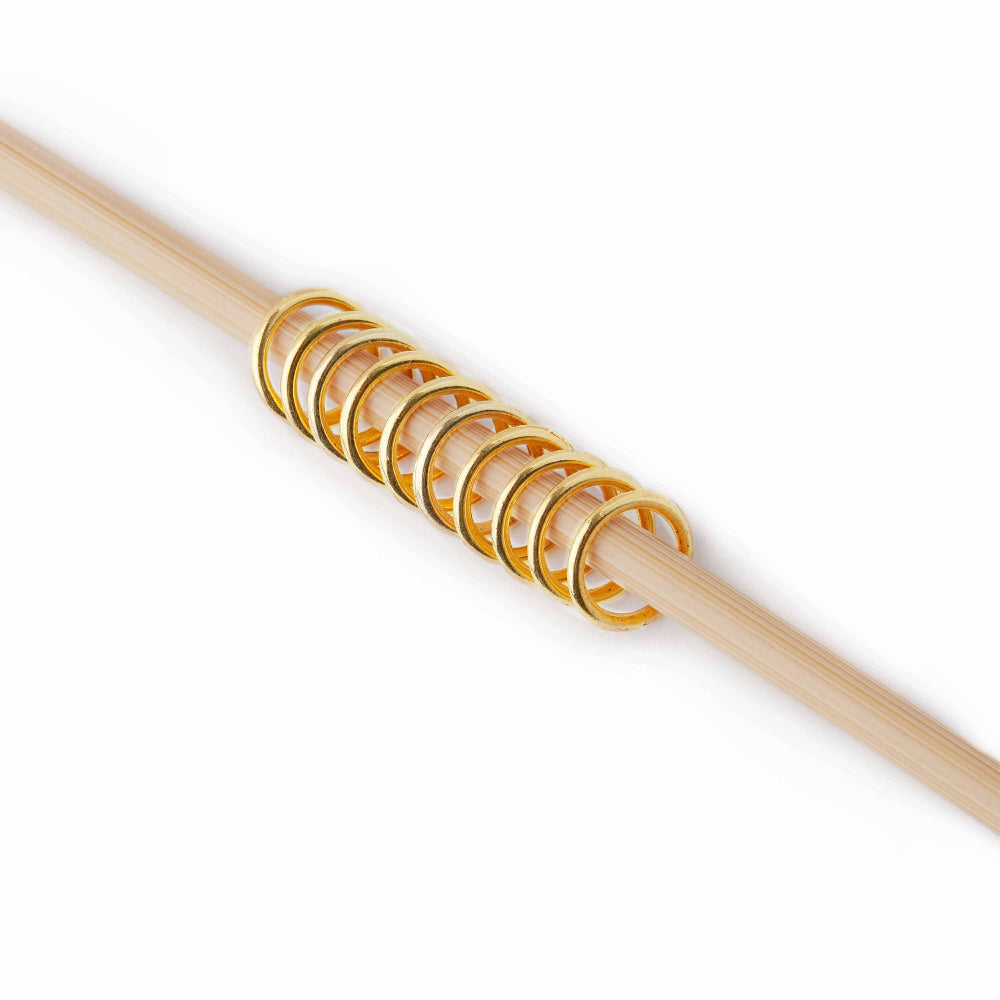 Wooden knitting needle with gold stitch markers on a white background