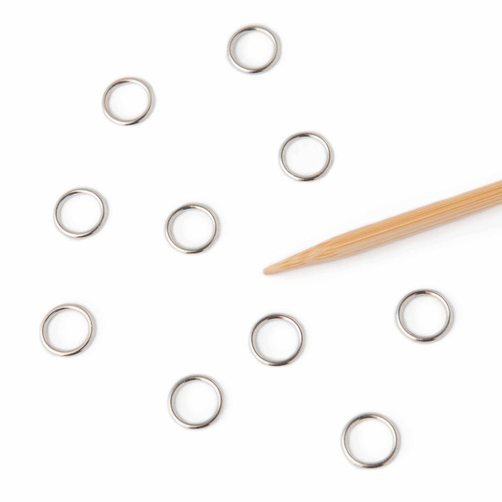 Silver stitch markers scattered on a white surface with a wooden tool.