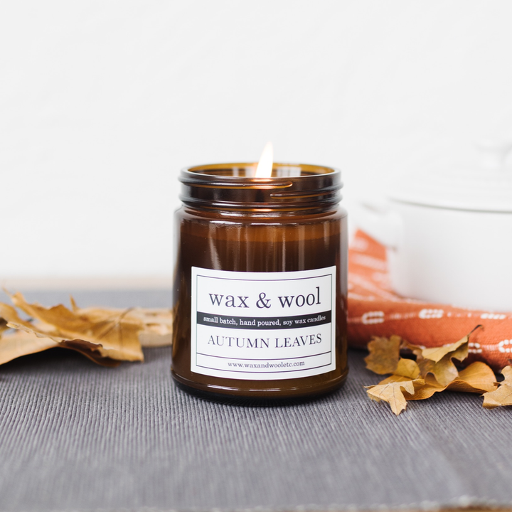 Candle in a brown jar labeled 'wax & wool' with 'Autumn Leaves' on a gray surface.