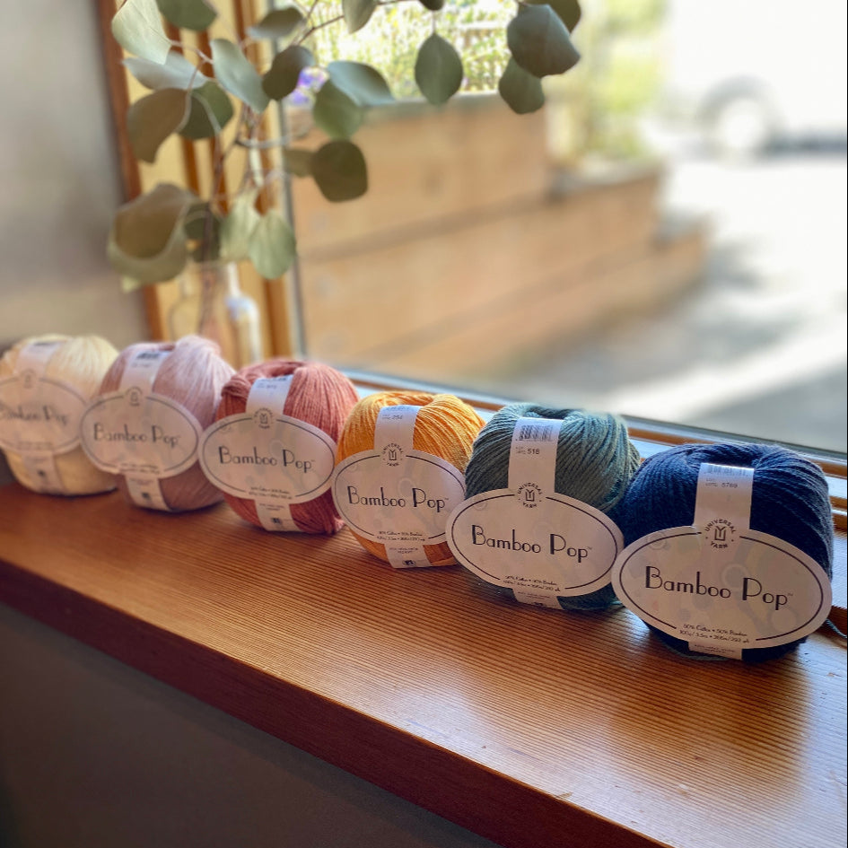 Six balls of bamboo pop yarn in various colors on a wooden surface with a blurred background