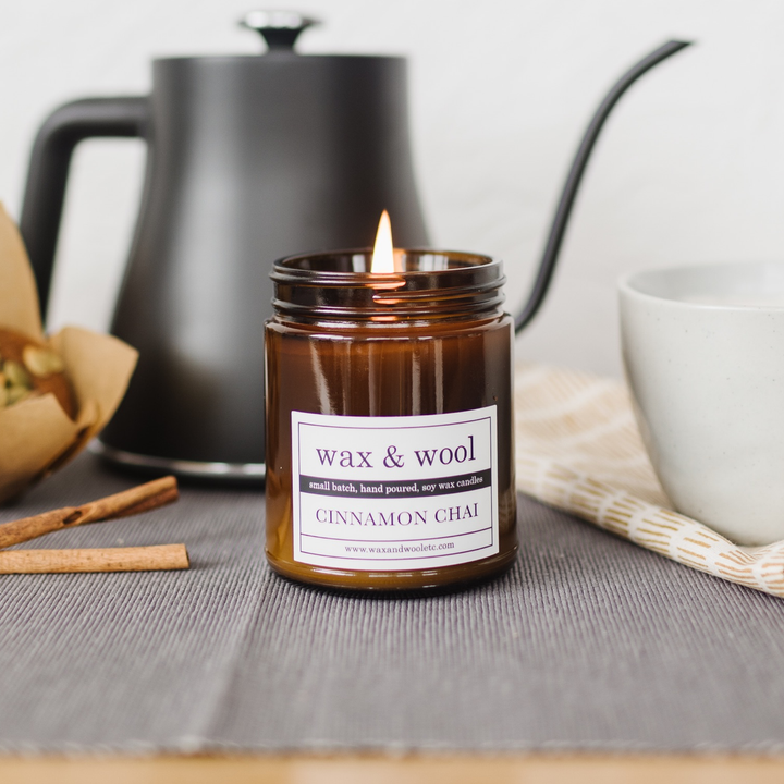 Candle labeled 'wax & wool' with cinnamon chai scent on a table with tea-making items.