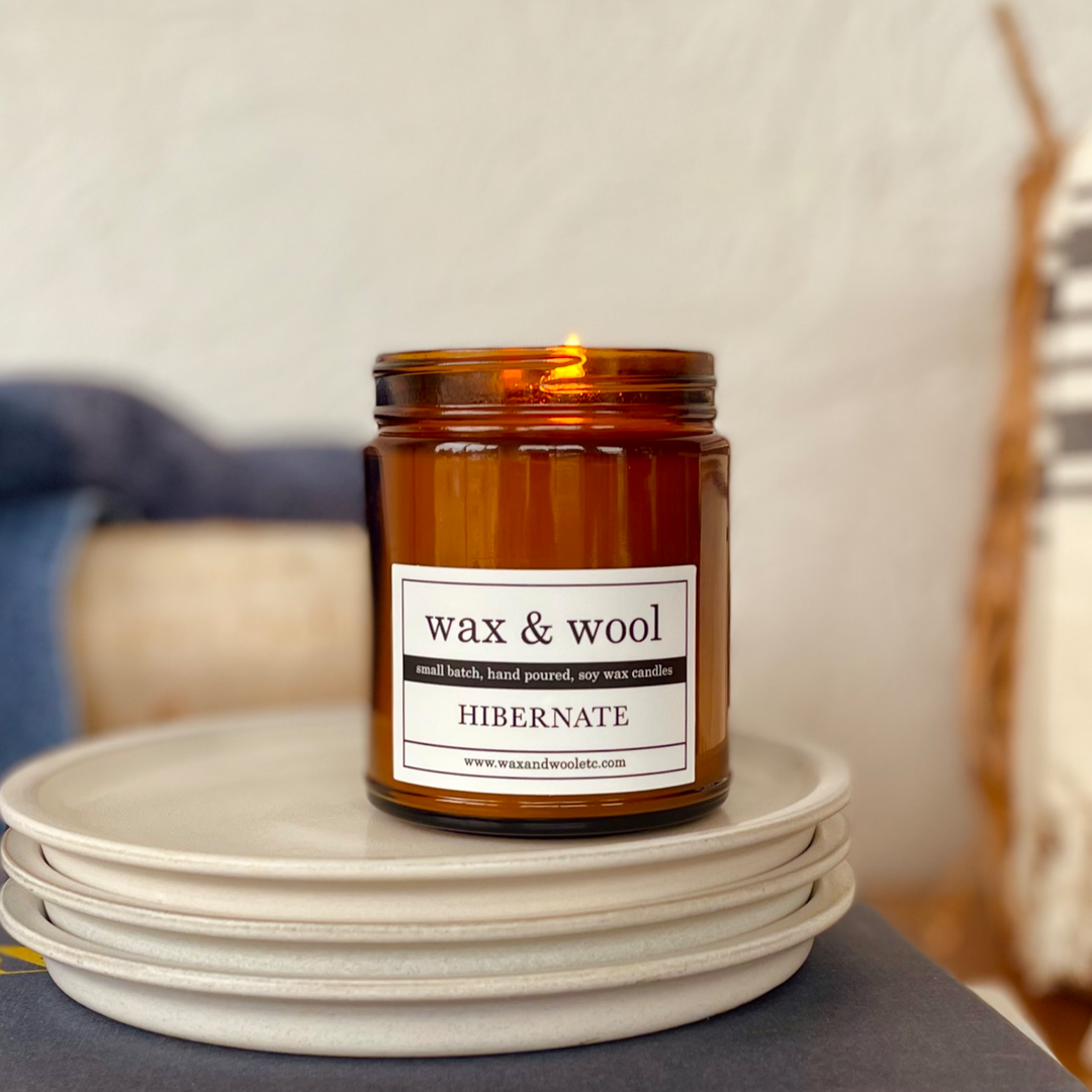 Candle in an amber jar labeled 'wax & wool' on a stack of white plates.