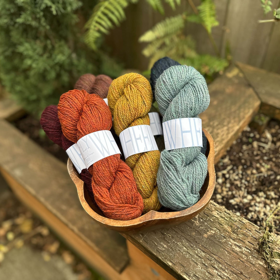Assorted skeins of FlyWheel yarn in a wooden bowl with a natural outdoor background