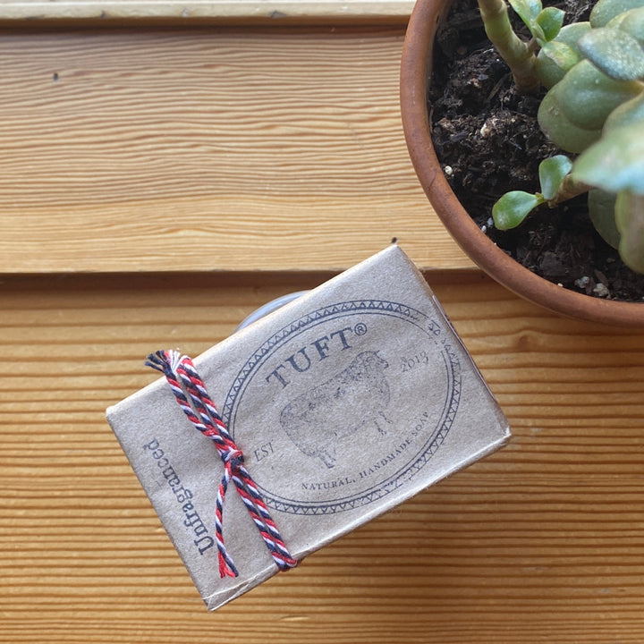 Box of TUFT products on a wooden surface with a potted plant in the background