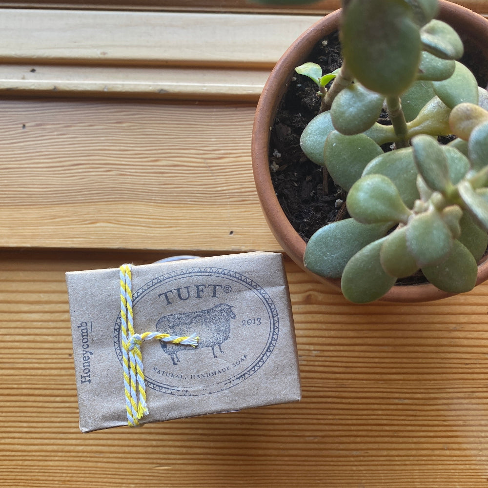 Bar of soap with a 'TUFT' label next to a potted succulent on a wooden surface