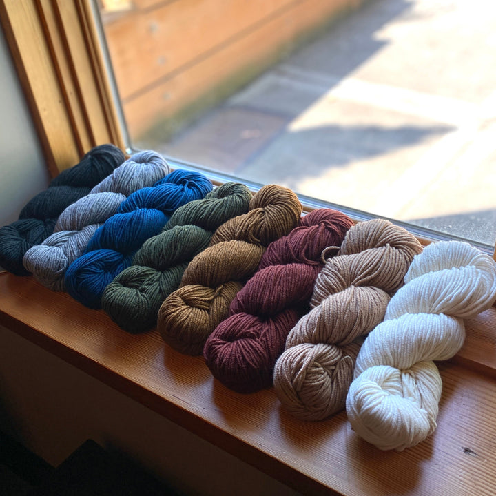 Assorted skeins of Tov yarn on a windowsill with a view outside.