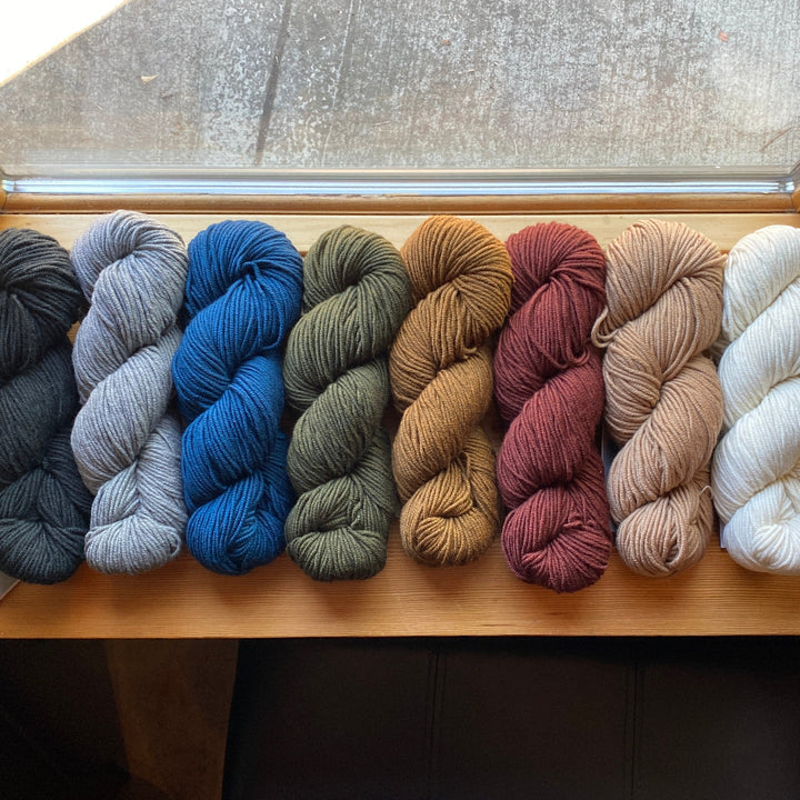 Row of yarn skeins in various colors on a wooden surface