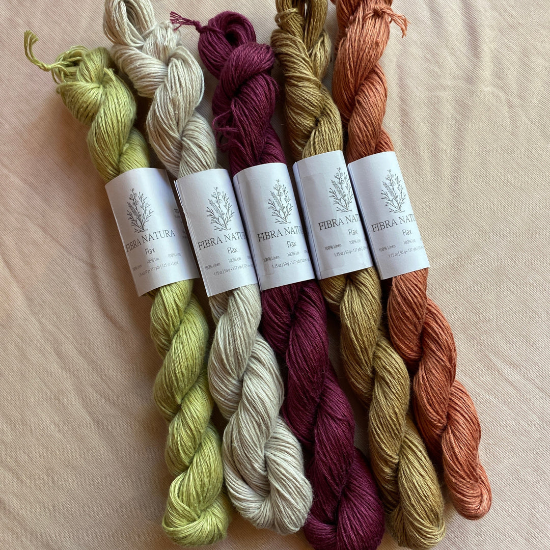 Five skeins of Flax yarn in green, white, purple, yellow, and orange on a beige surface with labels.