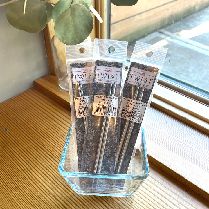 Three packages of 'Twist' brand products in a glass container on a wooden surface with a window in the background.