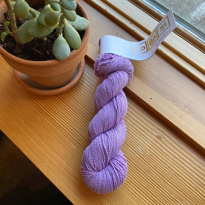 Purple skein of yarn with a label on a wooden surface next to a potted plant.