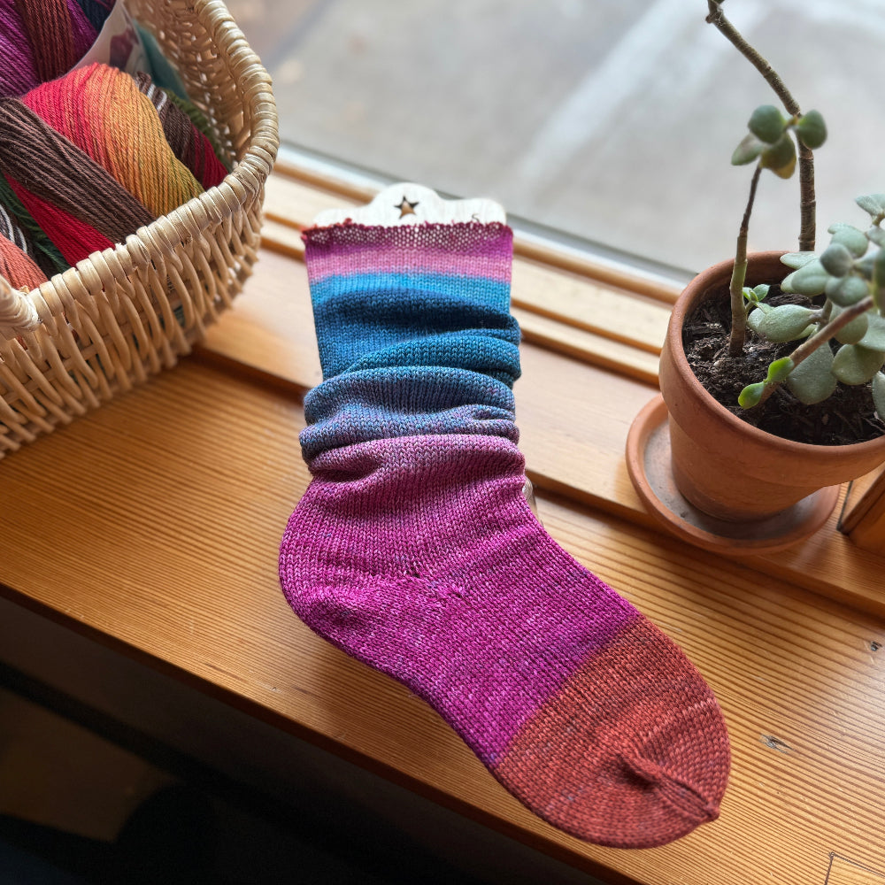 Colorful striped sock on a wooden surface with yarn and a plant in the background