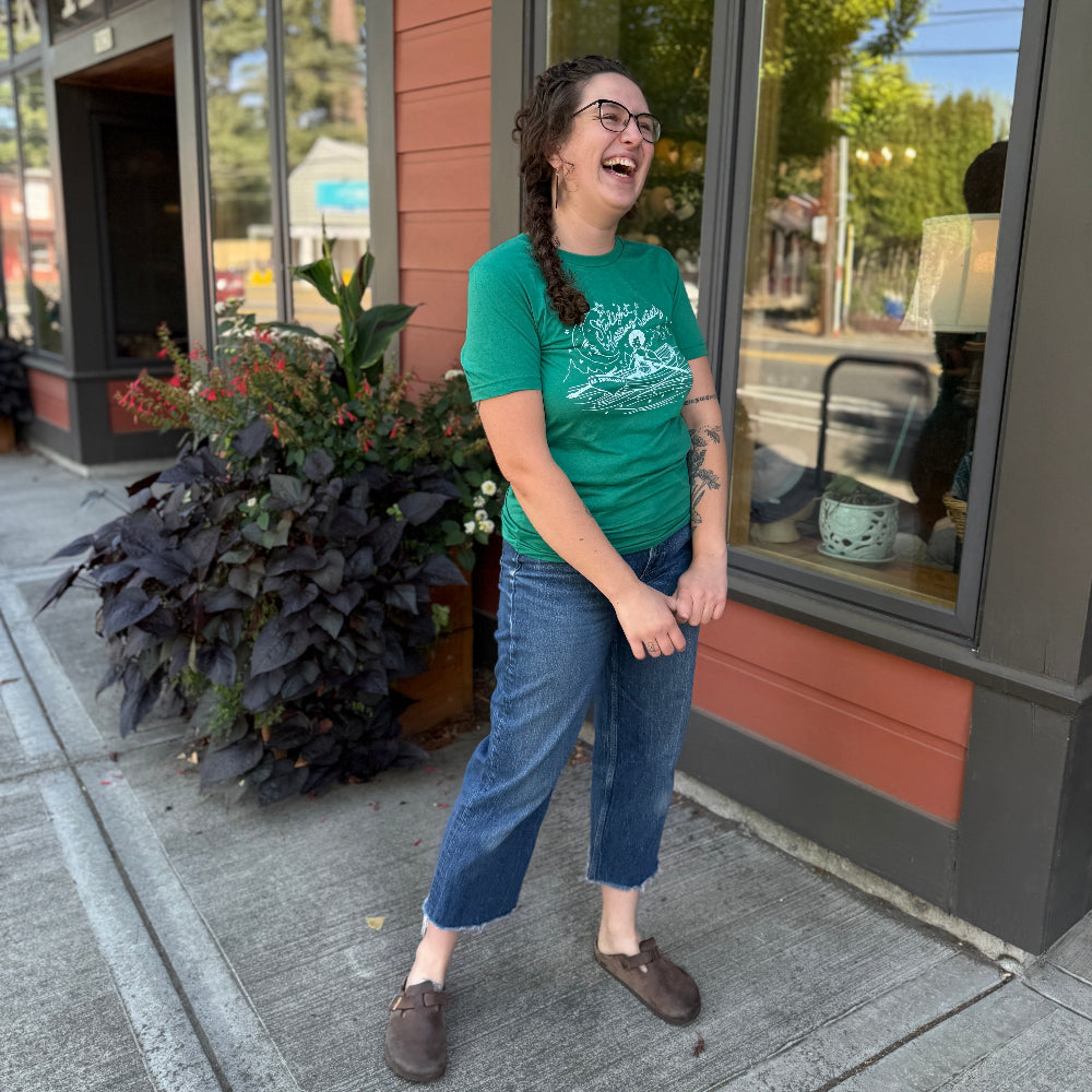 Person wearing a green t-shirt standing on a sidewalk in front of a store.