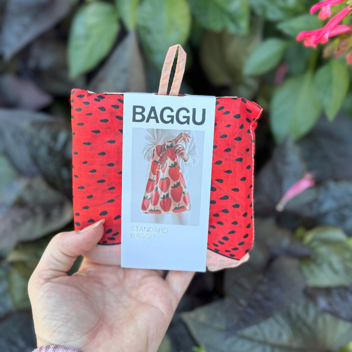 Red and black polka dot reusable bag with 'BAGGU' branding held against a leafy background.