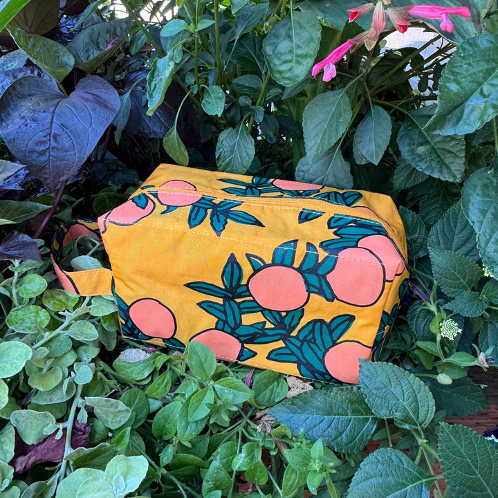 Yellow pouch with pink floral design placed among green plants