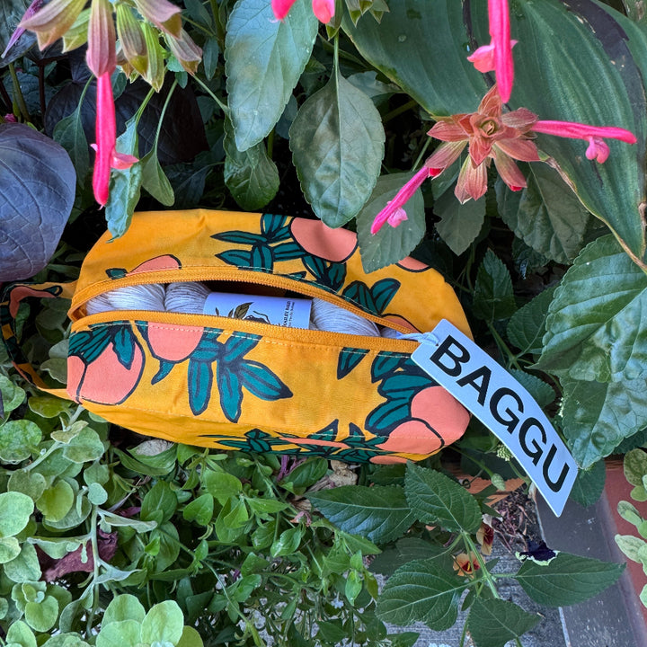 Yellow reusable bag with floral design and 'BAGGU' tag among green plants