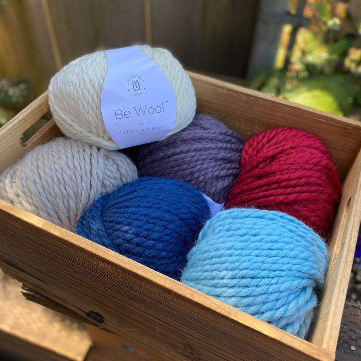 Box of colorful yarn balls with a 'Be Wool' label outdoors.