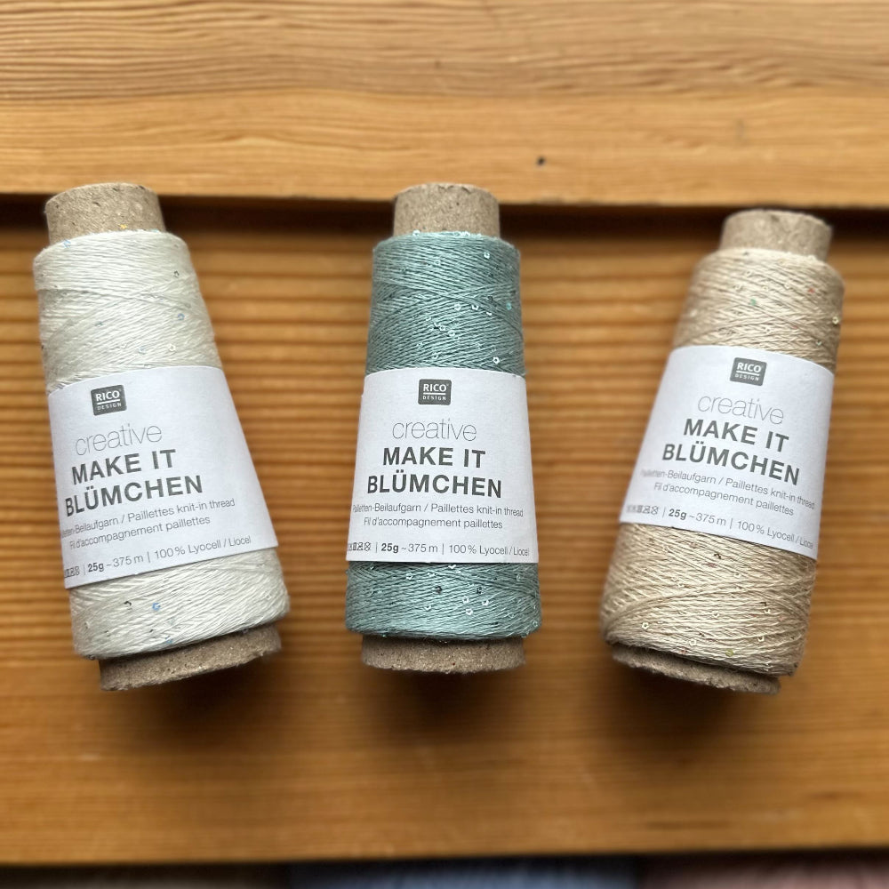 Three spools of yarn on a wooden surface with visible labels.