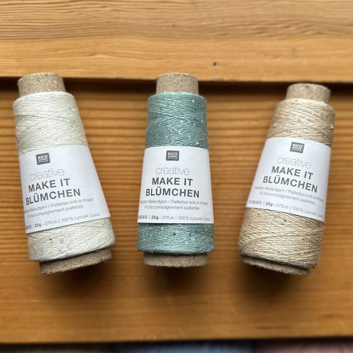 Three spools of yarn on a wooden surface with visible labels.