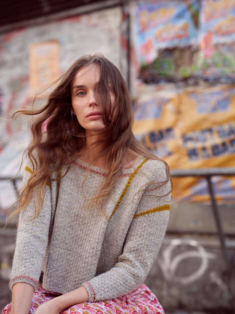 Woman wearing a patterned sweater sitting against a colorful graffiti wall.