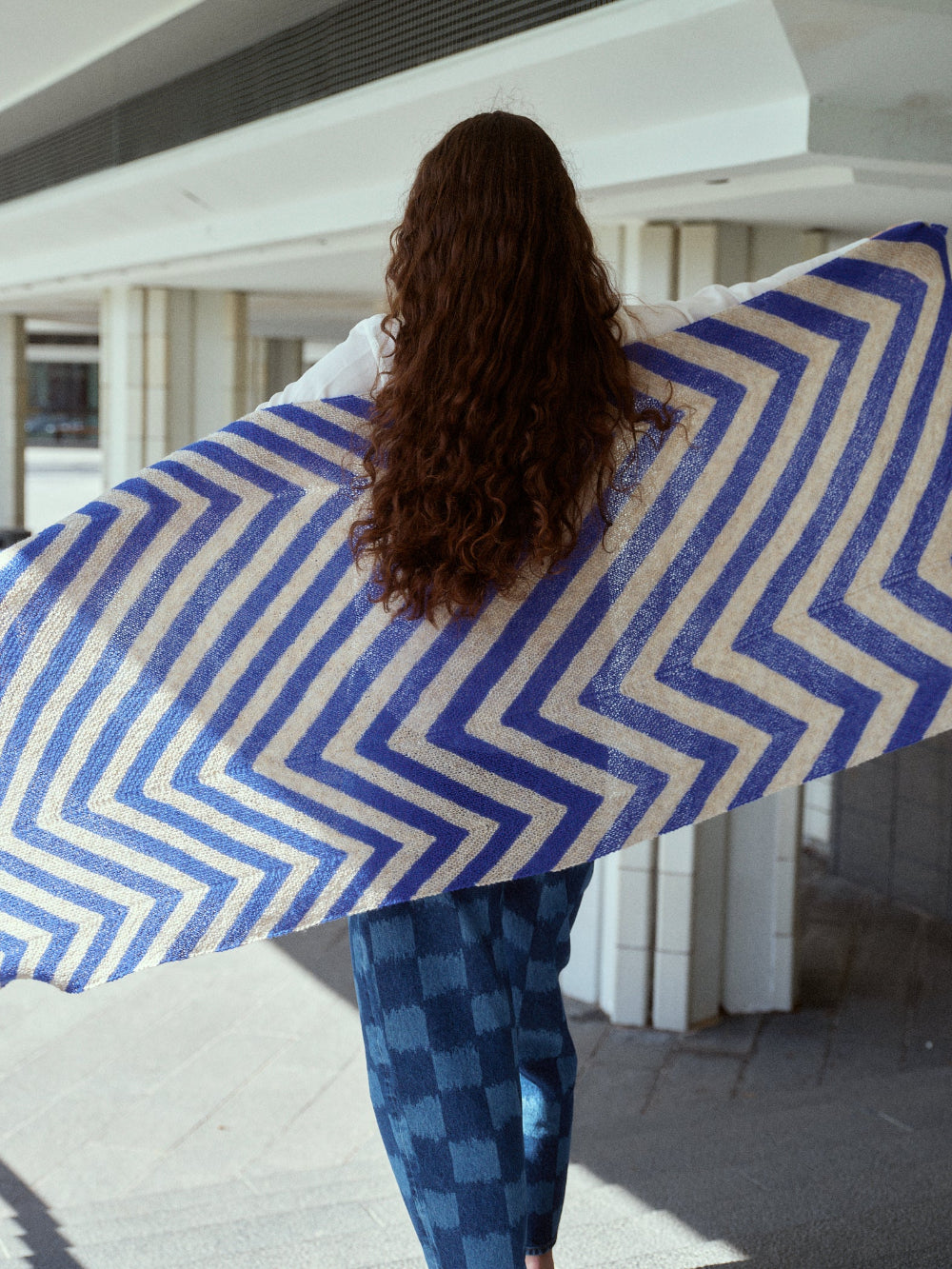 Person holding a large blue and white zigzag patterned blanket outdoors.