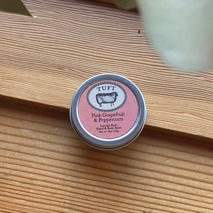 Small container of 'Pink Grapefruit & Peppercorn' body balm on a wooden surface with 'TUFT' branding.