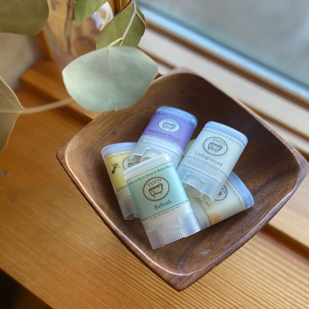 Tuft Hand and body balm with labels in a wooden bowl on a wooden surface.