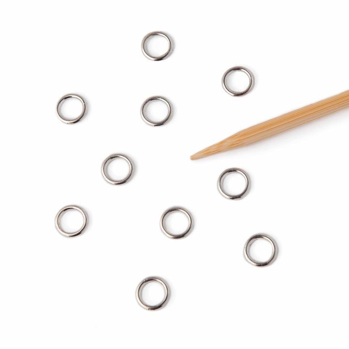 Silver jump stitch markers scattered on a white surface with a wooden tool.