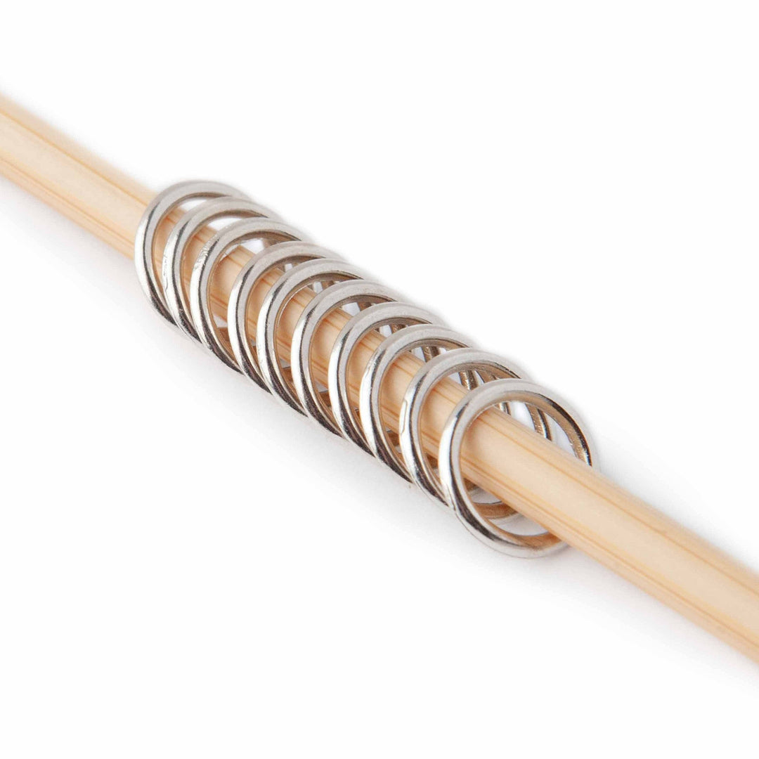 Wooden knitting needle with metal stitch markers on a white background