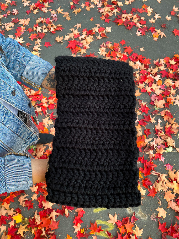 black crocheted scarf, outdoors, being held in outstretched hands on a background of red fallen maple leaves